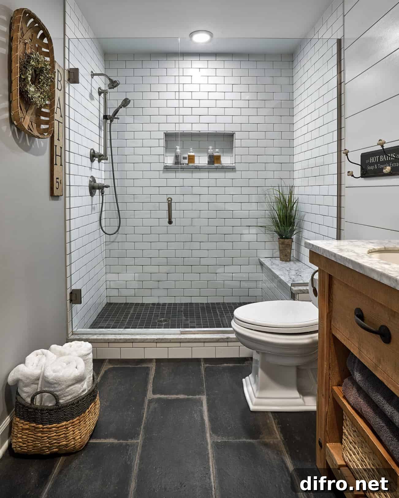 white subway tile farmhouse basement bathroom with wood vanity toilet grey slate floor tobacco basket hanging on wall basket of rolled towels