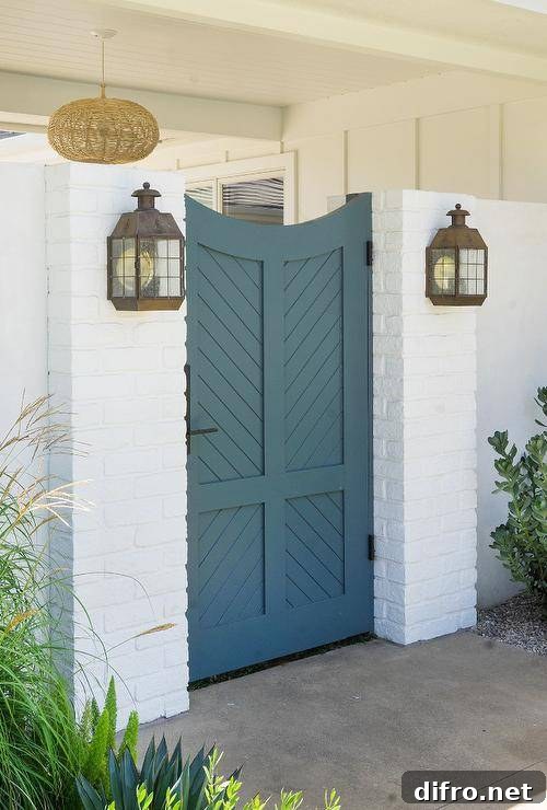 Blue wooden chevron gate door completed with oil rubbed bronze hardware illuminated by vintage sconces flanked by a white brick wall.