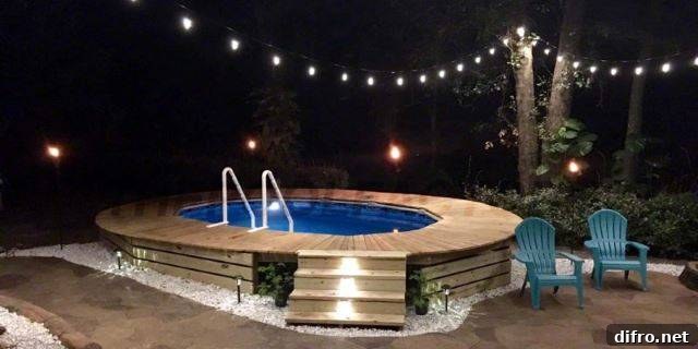 above ground pool oval shape with deck built around it at night with string lights