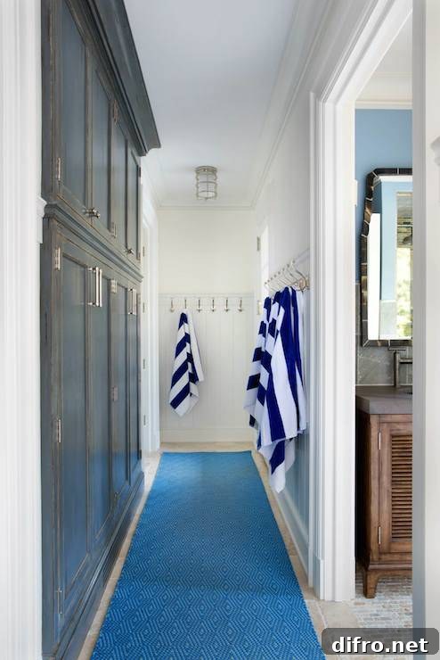 Beachy hallway with built-in dark stained mud room cabinets across from paneled walls lined with coat hooks