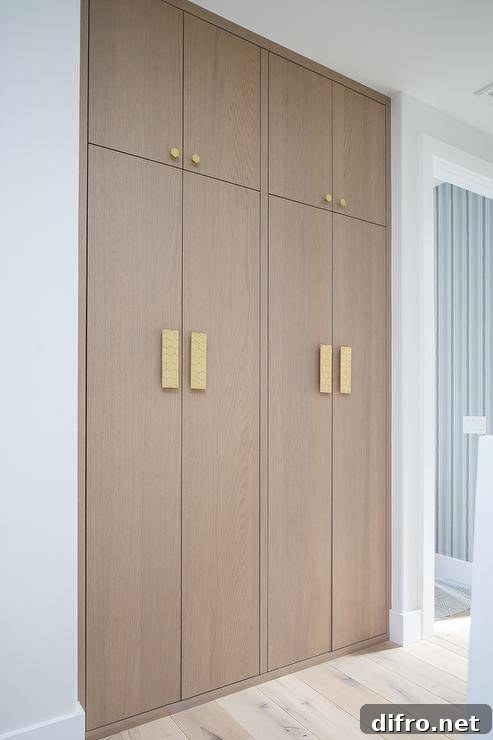 Brass hexagon hardware complements stacked floor-to-ceiling brown oak hallway cabinets