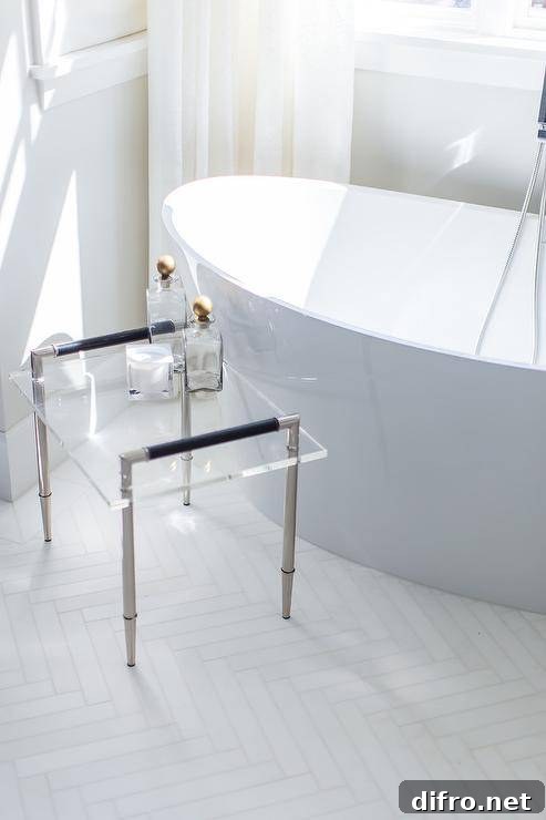 A nickel and lucite accent table beside a freestanding bathtub.