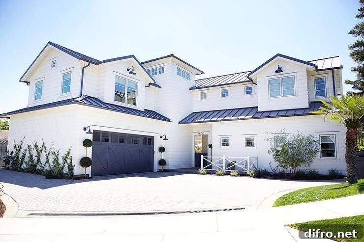 White and blue home with a blue garage door displaying topiaries and black vintage lamps on the sides. Navy roofing and white siding invite a modern farmhouse appeal to the home design.