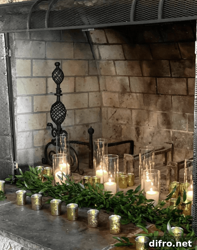 glass hurricane candles with greenery in a brick fireplace