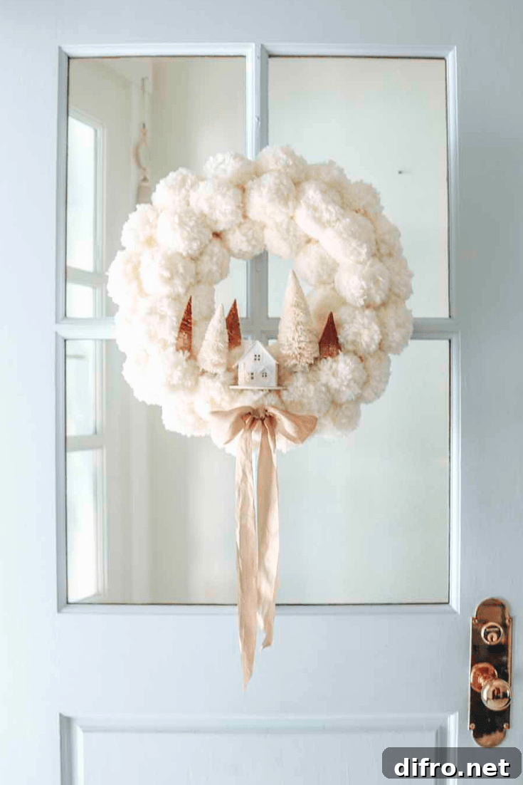 white pom pom christmas wreath with little white house and bottle brush trees