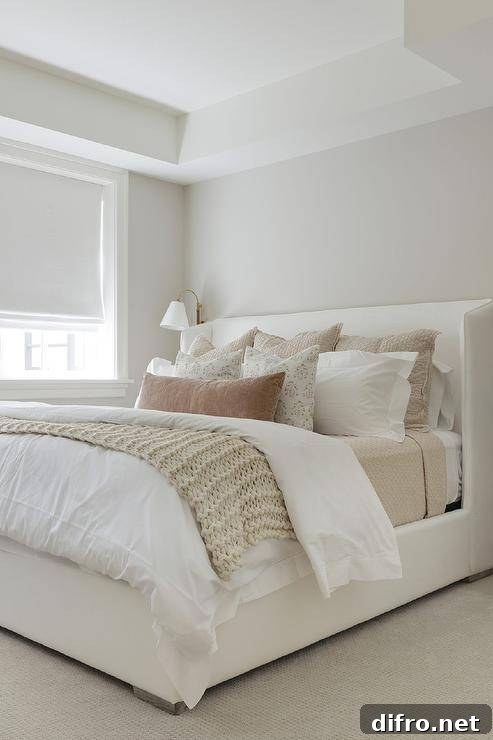 A white upholstered wingback bed is complemented with tan and brown layered pillows placed on white and tan bedding.