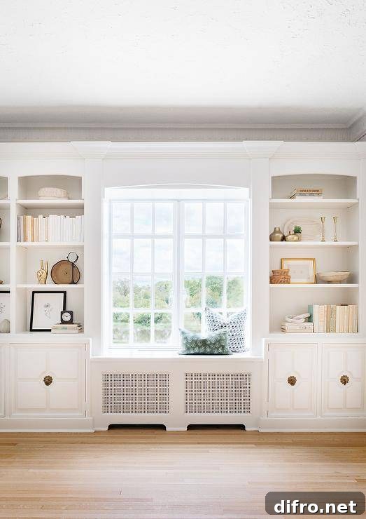 White styled shelves fixed over white cabinets with brass hardware flank a built-in window seat.