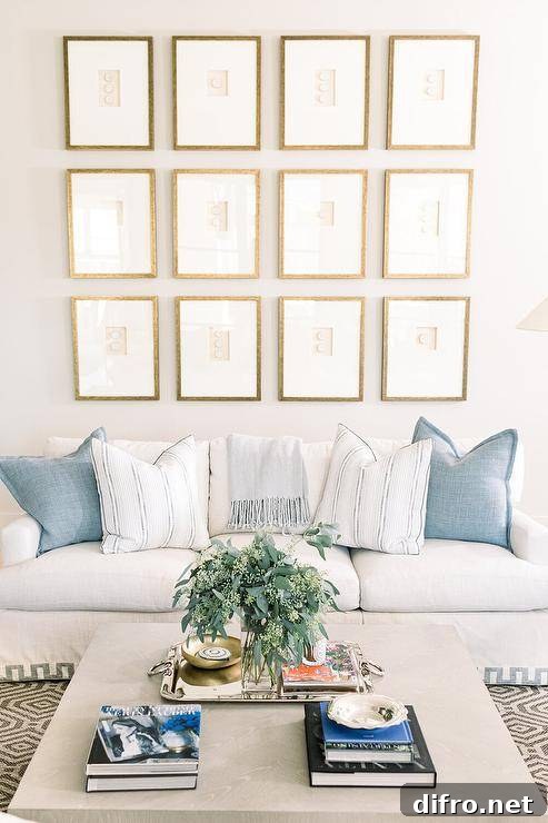 Gold framed gallery wall on a white wall adds a sophisticated appeal above a white sofa with Greek key trim and blue pillows.