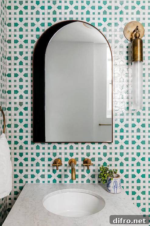 A brass and glass cylinder sconce beside an arched medicine mirror over a marble top vanity.