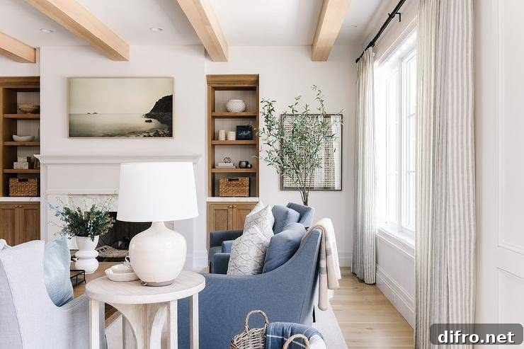 A cream lamp sits atop a round end table beside blue upholstered accent chairs under wood beams.