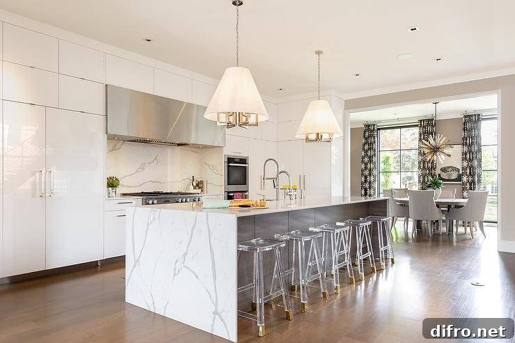 Stunning quartz waterfall island fitted with backless ghost saddle stools under conical drum pendants.