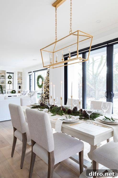 Dining room features a Christmas garland and acorn runner on a long off white dining table with off white fabric dining chairs illuminated by a Darlana rectangular linear lantern.