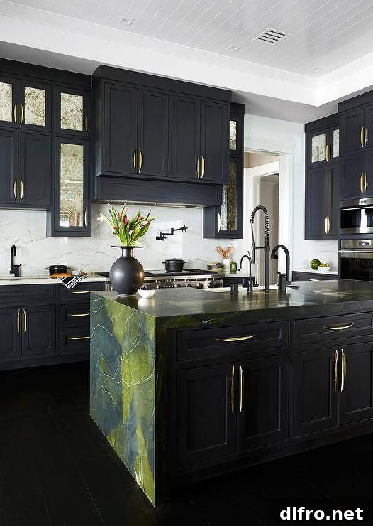 Contemporary kitchen features a green and black marble waterfall island with a matte black pull out kitchen faucet, and antiqued mirrored black cabinets with modern brass pulls topped with ivory and black marble.
