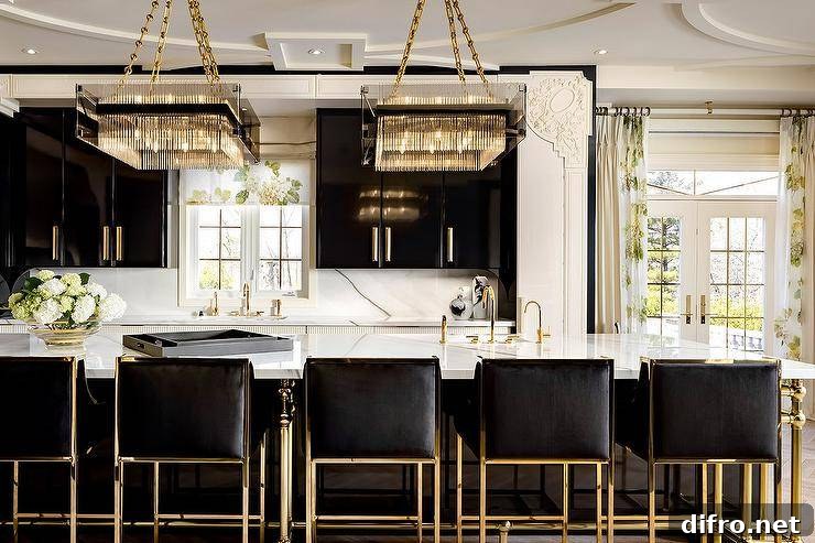 Contemporary black and white kitchen features black cabinetry with brass pulls and gold and black island stools at a marble top island lit by square crystal chandeliers.