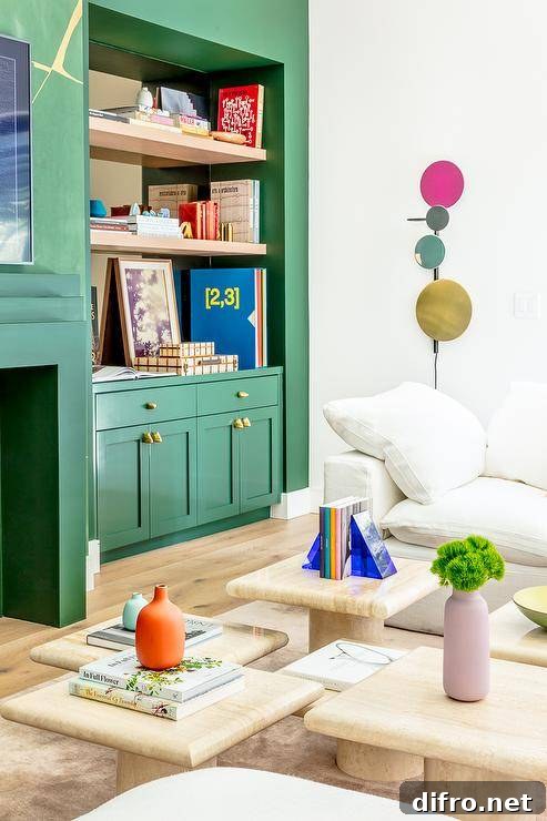 Green shaker lacquered living room cabinets adorned with brass knobs and fitted beneath inset blond wood floating shelves mounted against a mirrored backsplash and beside a green art deco fireplace.