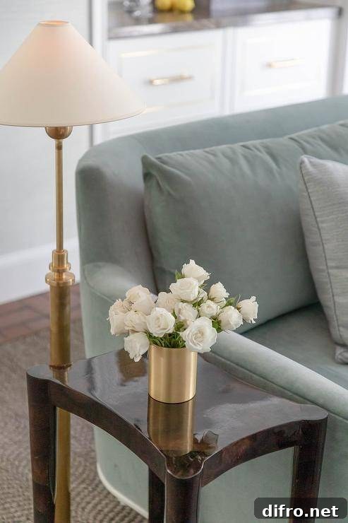 Living room features a sage green velvet sofa with a brown lacquer end table illuminated by an antique brass floor lamp.