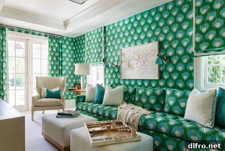 Bold blue and green print wallpaper complement a green and blue sofa accented with ivory and green pillows and matched with two ivory ottomans and a cream wingback chair.