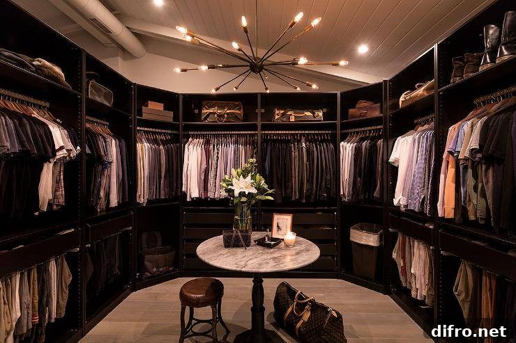 Men’s walk-in closet with luggage, round accent table and sputnik chandelier.