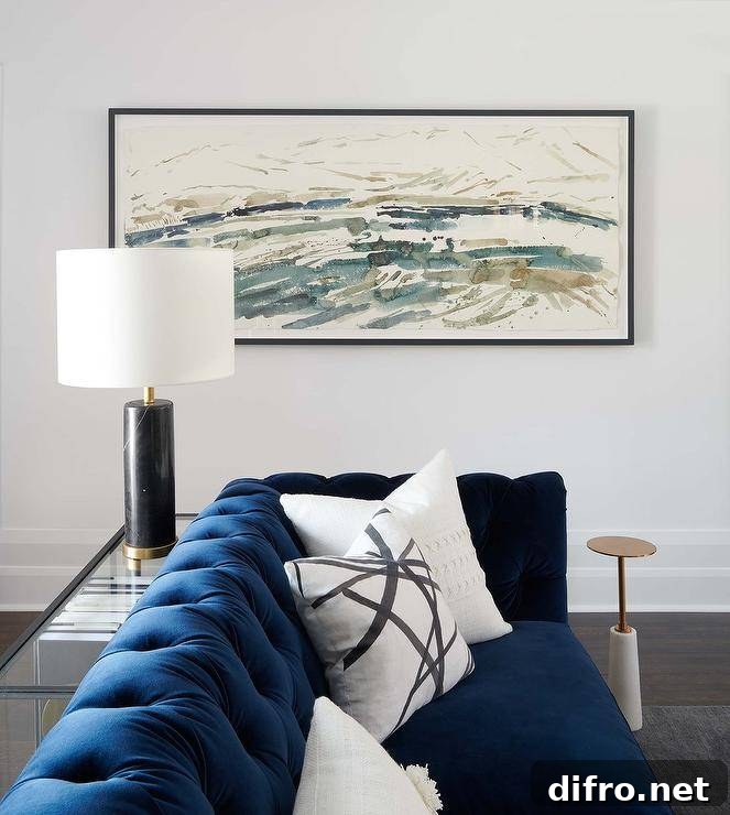 Blue velvet tufted couch with white pillows and a sofa table lit by a black lamp.