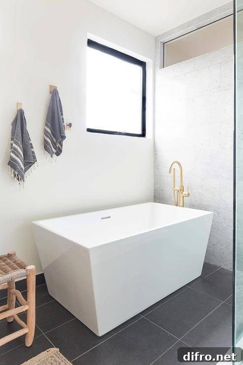 Bathroom features a modern white freestanding rectangular bathtub with polished brass gooseneck faucet tub filler on a black tiled floor.