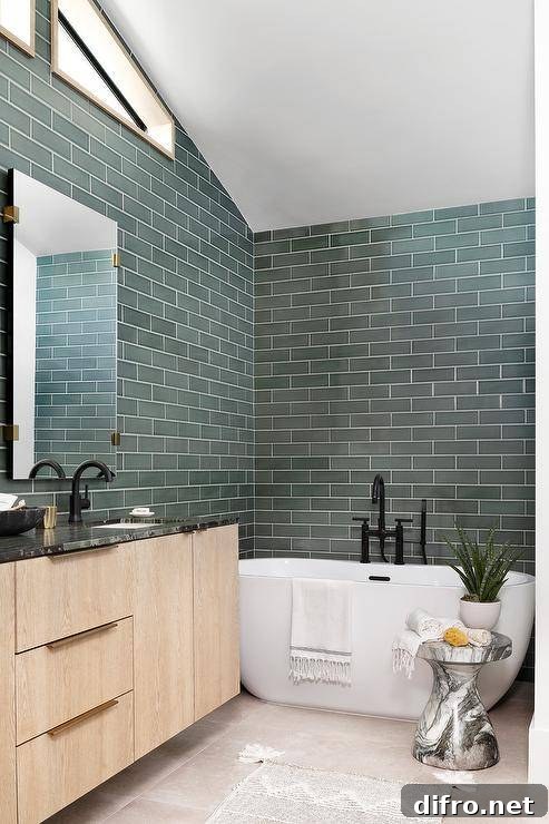 Green tiled bathroom walls complement a white oval freestanding bathtub paired with a matte black tub filler.