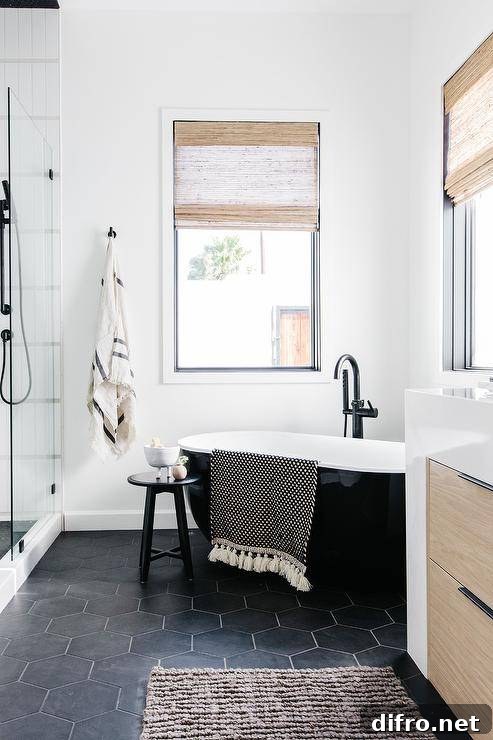 Black and white modern bathroom designed with a catty corner tub on black hexagon floor tiles and a matte black gooseneck tub filler.