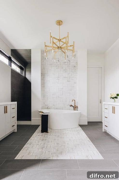 A brass chandelier illuminates a luxurious bathroom featuring an oval freestanding bathtub with a catty corner aged brass floor mount tub filler.