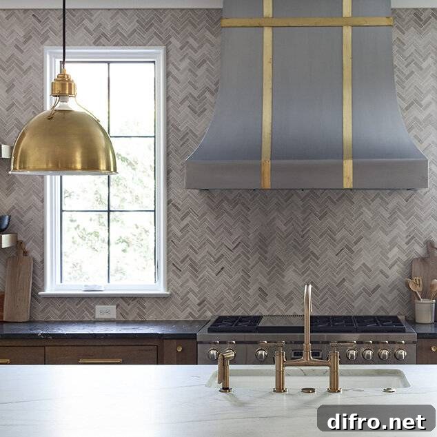 A stainless steel French range hood with brass straps over a stainless oven range and gray marble tiles