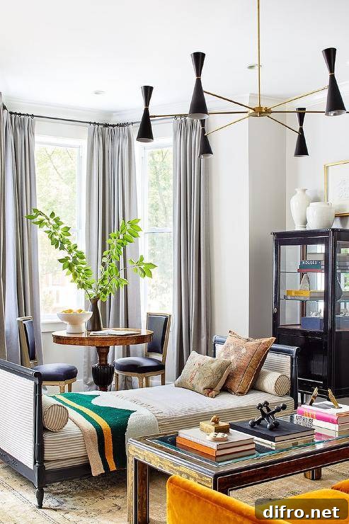 Contemporary living room designed with a black French daybed and stripe bolster pillows on a gray and tan rug in front of a bay window with black French chairs and an antique table.