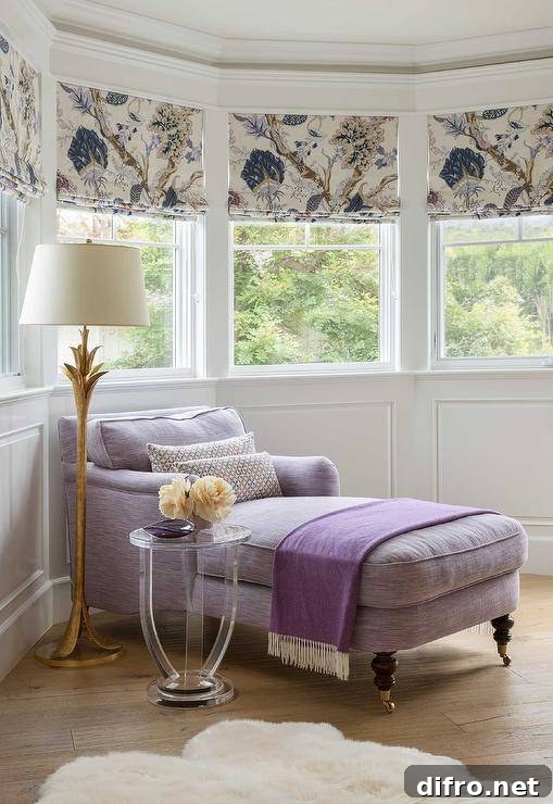 Purple chaise lounge in the corner of a master bedroom bay window beside a gold leaf floor lamp and a round lucite accent table. Bay window wainscoting adds a decorative touch to the walls with windows dressed with purple floral shades.