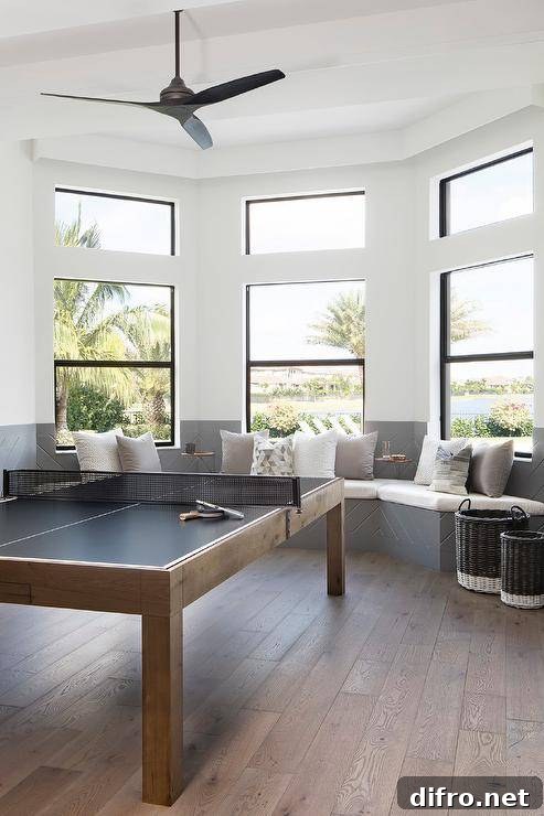 Chic game room features a bay window fitted with gray window seats alongside white and gray cushions. A modern ping pong sits in front of a bay window.