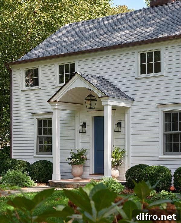 A beautiful white home boasting white siding and a blue front door positioned beneath a portico lit by an oil rubbed bronze carriage sconce.