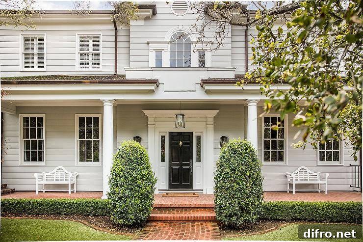 Light gray home siding featuring doric front porch column, a black front door and red brick pavers.