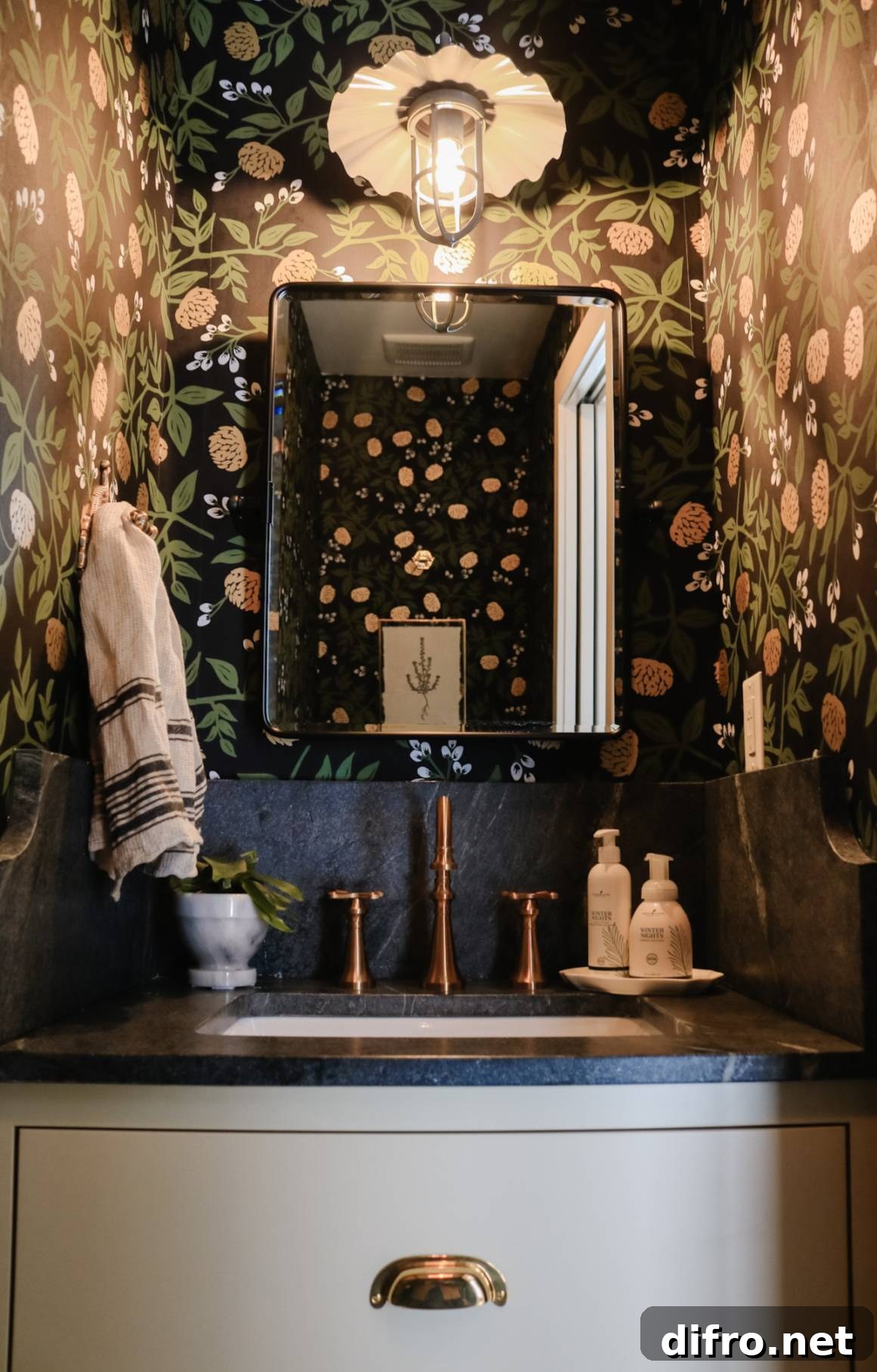 dark floral wallpaper on walls and ceiling surrounding dark bathroom vanity with black mirror