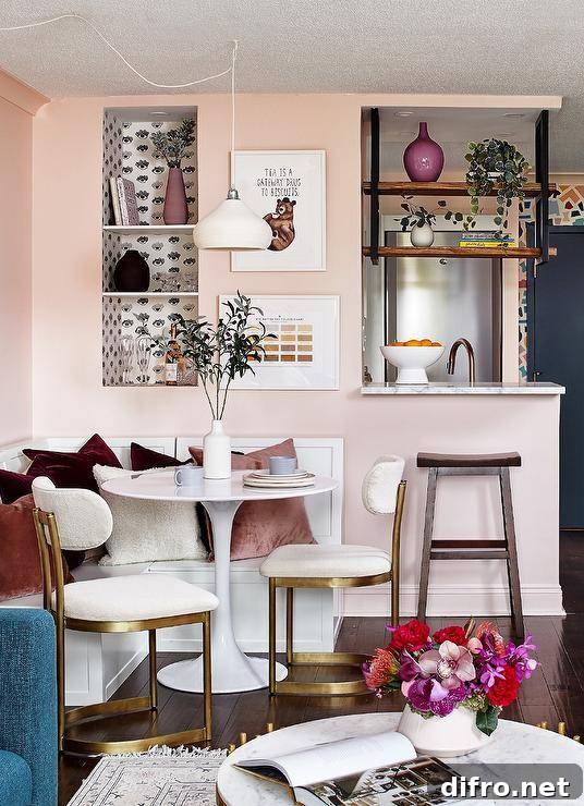 Small apartment features a white l-shaped dining bench fixed against a pink wall and topped with pink and velvet pillows.