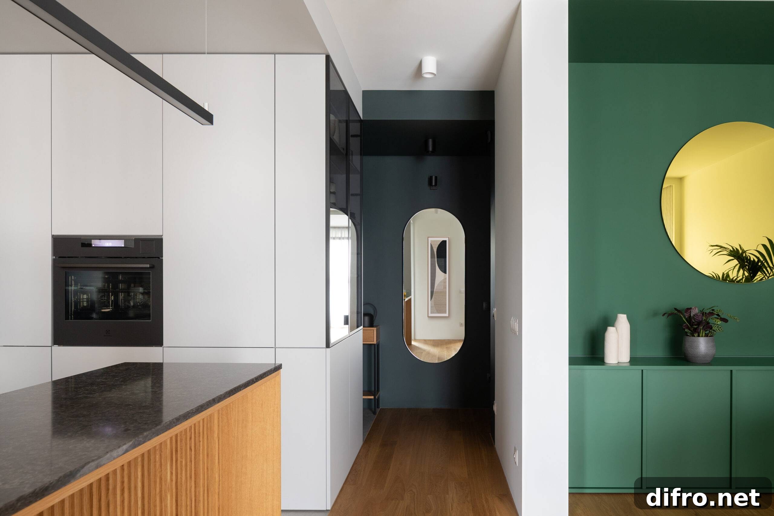 hallway with oval mirror at the end, green accent wall to the right and white kitchen to the left