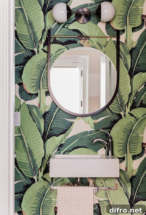 Jungle palm leaf wallpaper in a powder room with a wall-mount sink and round mirror.