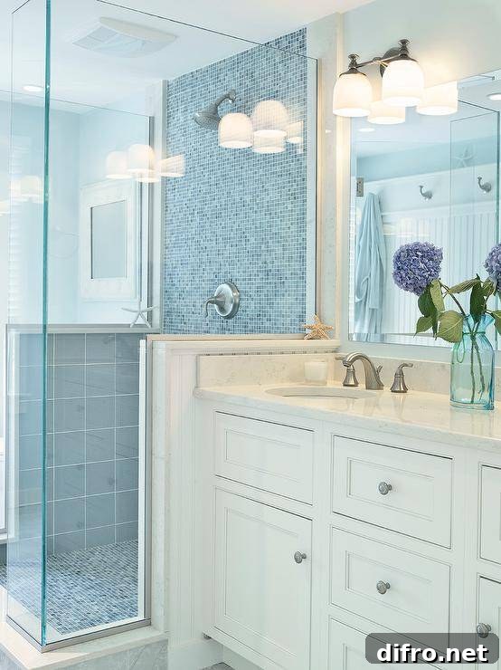 Beachy bathroom features a large walk-in shower centered against the vanity wall boasting sky blue tiled sides and a blue glass mosaic tile wall and shower floor beside an ivory shaker vanity adorned with brushed nickel pulls alongside a white quartz counter finished with a beveled vanity mirror above lit by a frosted glass vanity light.