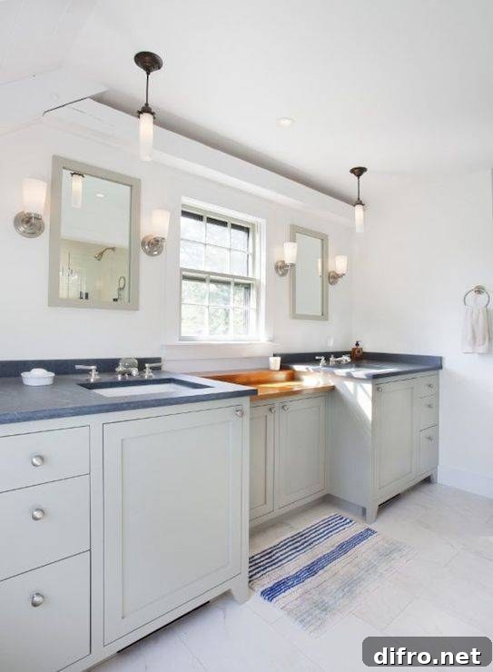 Coastal bathroom with gray built-in vanity accented with brushed nickel hardware alongside gray countertops which frame undermount porcelain sinks below light gray vanity mirrors illuminated by nickel uplight wall sconces.