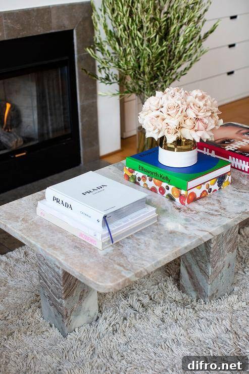 A pink and gray marble coffee table sits on a gray shag rug with flowers and books arranged on top