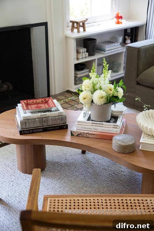 On a light gray rug, a vintage kidney shaped coffee table is accented with stacked books in front of a dark gray sofa.