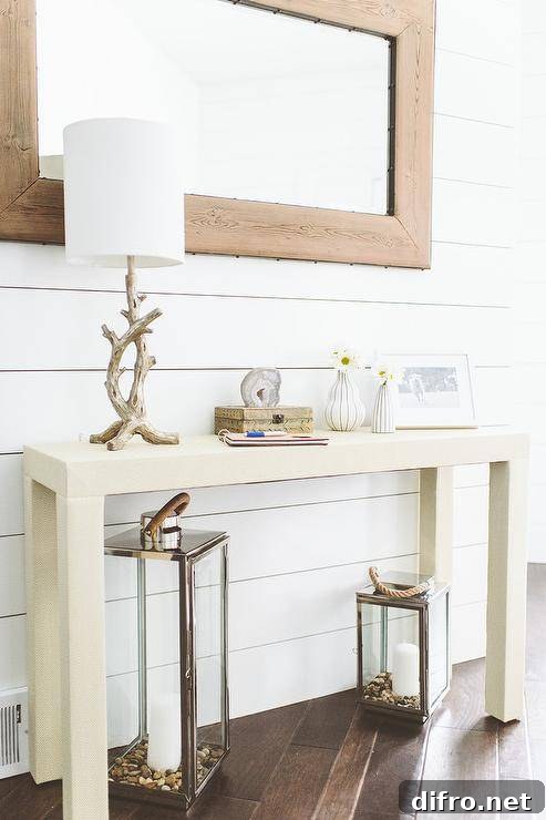 Beach entryway with driftwood table lamp, framed photo and urchin bud vase below a rustic wood mirror.