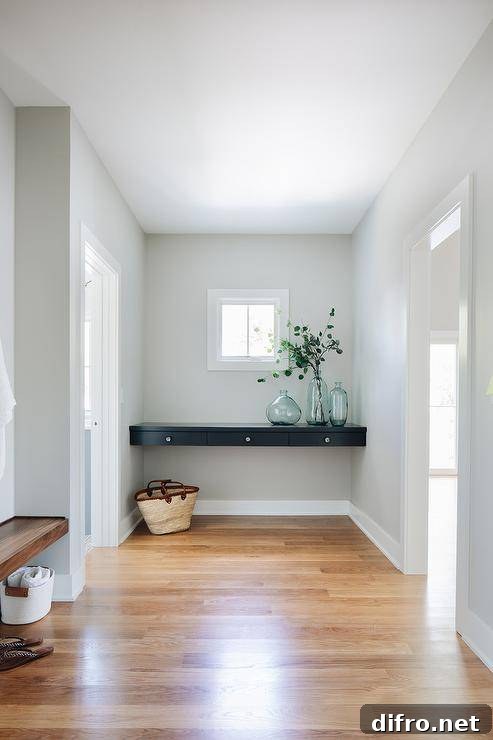 Entryway designed with a black floating console table displaying recycled glass vases boasting gray painted walls and wood floors.