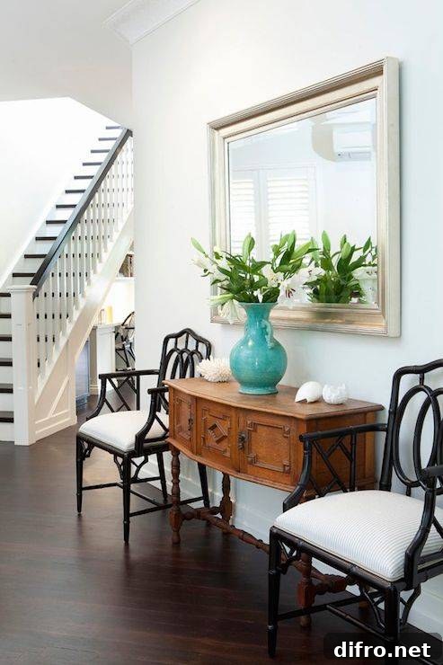 Beautiful foyer with vintage console with drawers topped with seashells and a turquoise urn filled with white lilies in front of a silver leafed mirror.