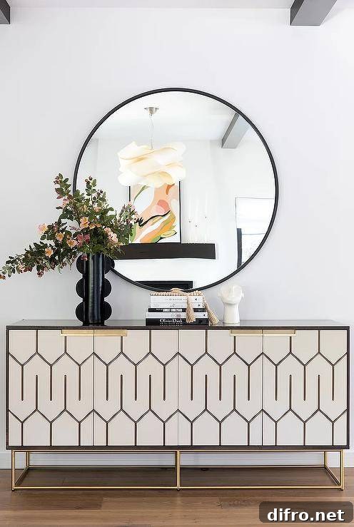 White and gold credenza under a round black mirror with a black vase.