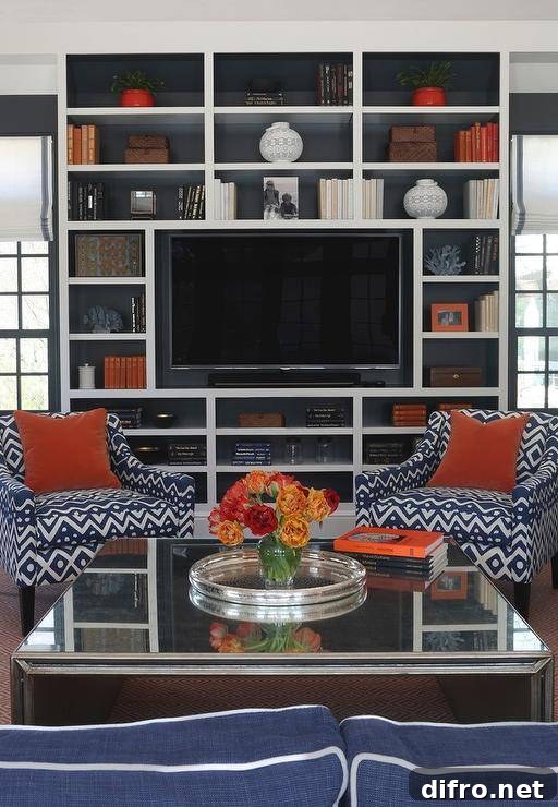 Blue and orange living room features a mirrored waterfall cocktail table and a pair of blue geometric accent chairs placed before floor to ceiling built in media unit.
