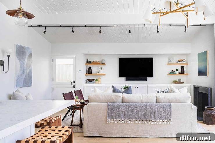 Living room features a natural linen sofa facing built in TV cabinets with wooden shelves, illuminated by track lights.