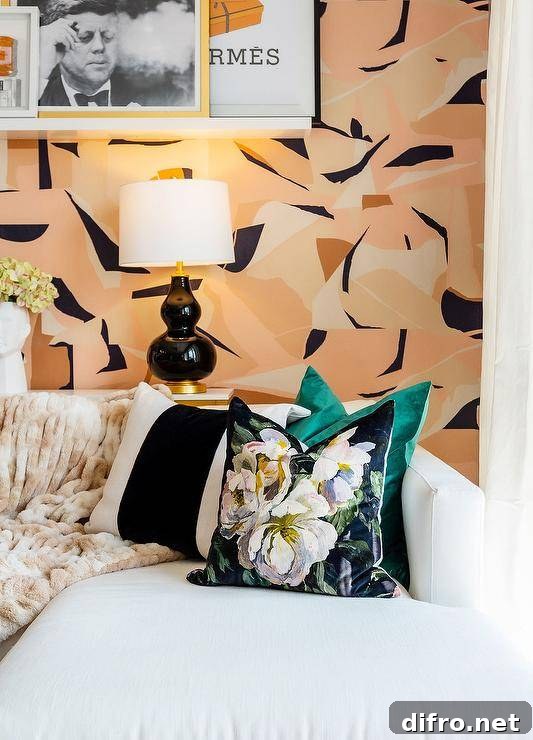 A white couch accented with black striped pillows is positioned beneath a floating picture shelf mounted to a wall covered in pink and black geometric wallpaper.
