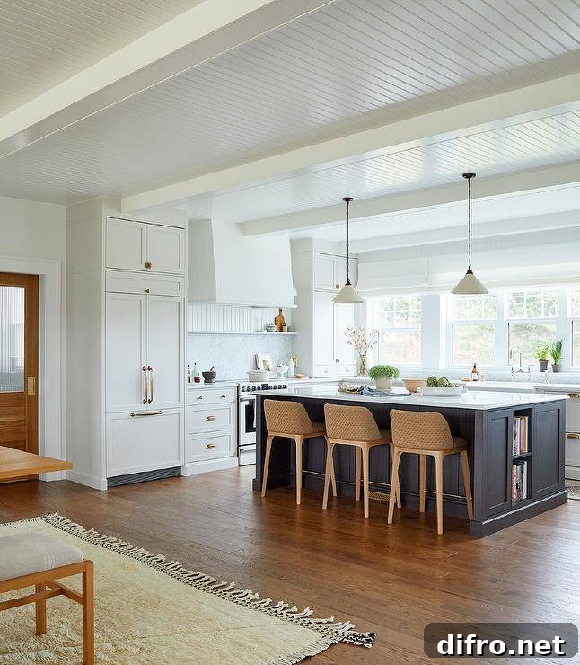 White u-shaped kitchen is contrasted with a black island fitted with cookbook shelves and seating brown woven stools at a white and gray marble countertop.