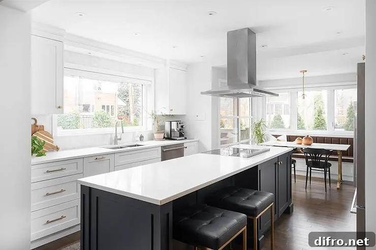 Spacious kitchen features black nuevo chi stools at a black and white island with an induction cooktop under an island hood and white cabinets with long brass pulls.